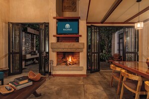 A cozy living room with a fireplace, a television mounted above it, and a dining area with wooden furniture. - Piemonte Casa (Concepción de Ataco)