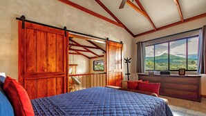 Une chambre avec un grand lit, des portes coulissantes en bois, une vue sur une montagne et une fenêtre avec des rideaux.