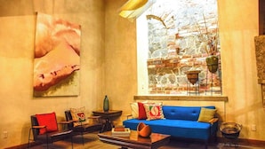 Un salon chaleureux avec un canapé bleu, une table basse et une grande fenêtre donnant sur un mur de briques et des plantes.