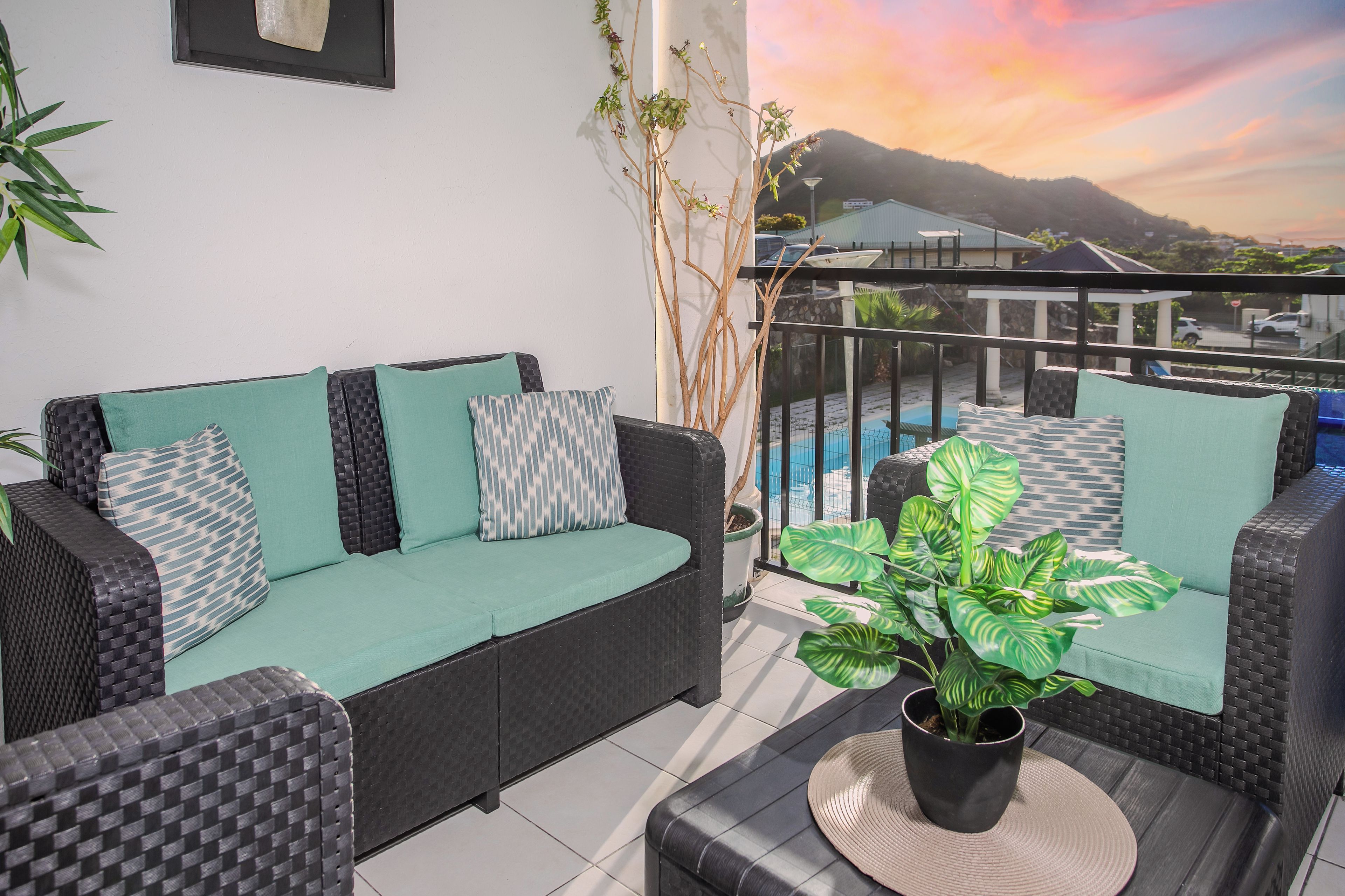 Un balcon avec un ensemble de meubles de salon, un pot de fleurs et une vue sur une montagne et un coucher de soleil.