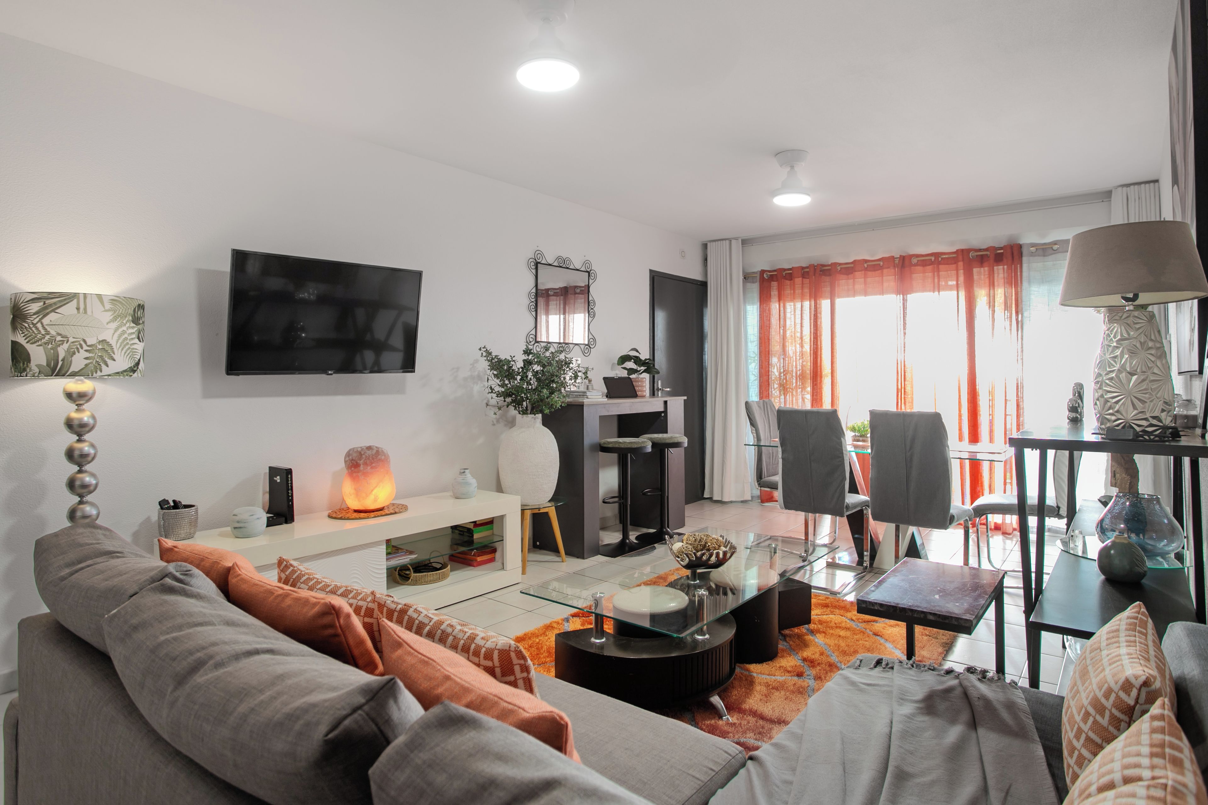 Ein modernes Wohnzimmer mit Flachbildfernseher, Kamin, Essbereich mit Stühlen und einem großen Fenster mit Vorhängen.