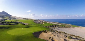A golf course with a bunker, a flag, and a distant mountain.