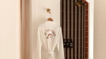 A white robe hanging on a wooden hanger in a bathroom with a tiled floor and a shower area with a striped glass door.