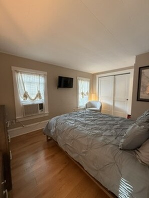 A bedroom with a bed, a chair, a TV, and a window with curtains.