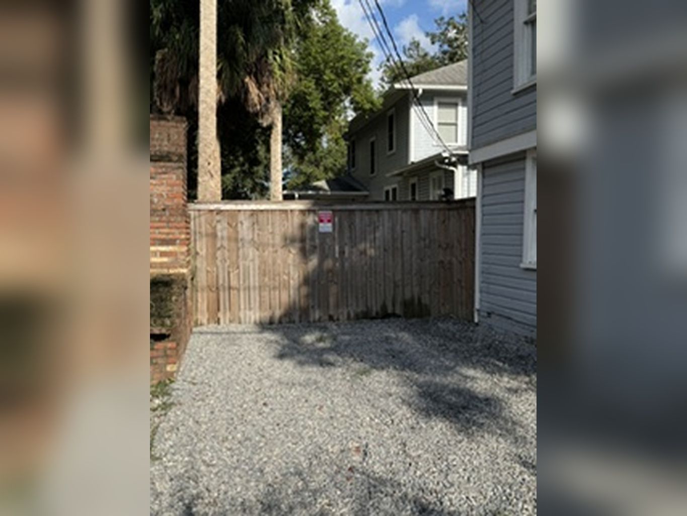 Il s’agit d’une propriété résidentielle avec une allée en gravier menant à un portail en bois, un mur en briques et une maison dont l’extérieur est recouvert de bardage gris.