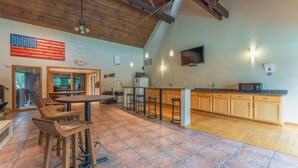A spacious kitchen with wooden cabinets, a large island with bar stools, a ceiling fan, and a mounted TV. - Beautiful Lake Views w/ Boat Slip! (Osage Township)