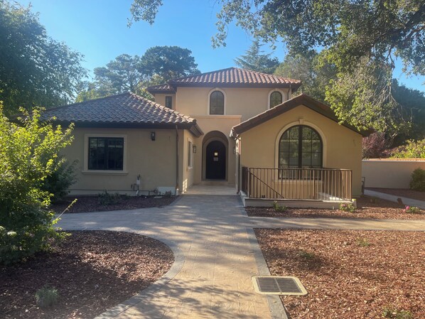 A two-story house with a tiled roof, a front porch, and a small garden area.