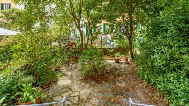 A stone pathway leading through a lush garden with various potted plants and trees. - La Margherita by MMega (Coverciano)