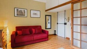 A room with a red sofa, wooden flooring, a white cabinet, and a sliding door with frosted glass panels.