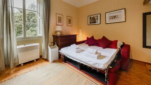 A bedroom with a bed, a heater, a lamp, and framed pictures on the wall.