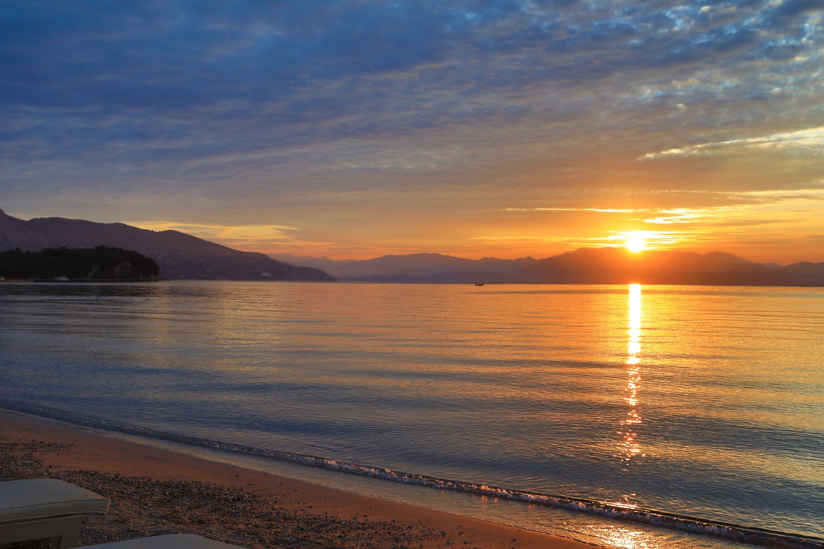 A calm lake at sunset with mountains in the background.