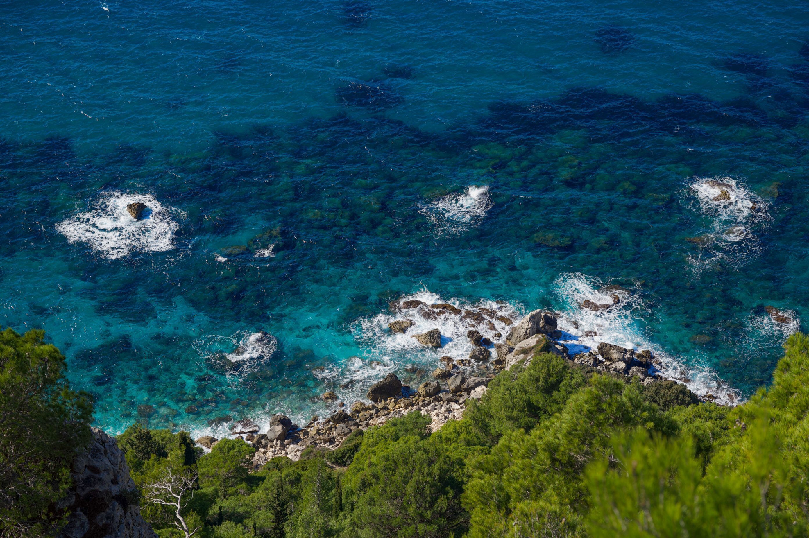 A coastal landscape with clear turquoise waters, rocky outcrops, and dense green vegetation.