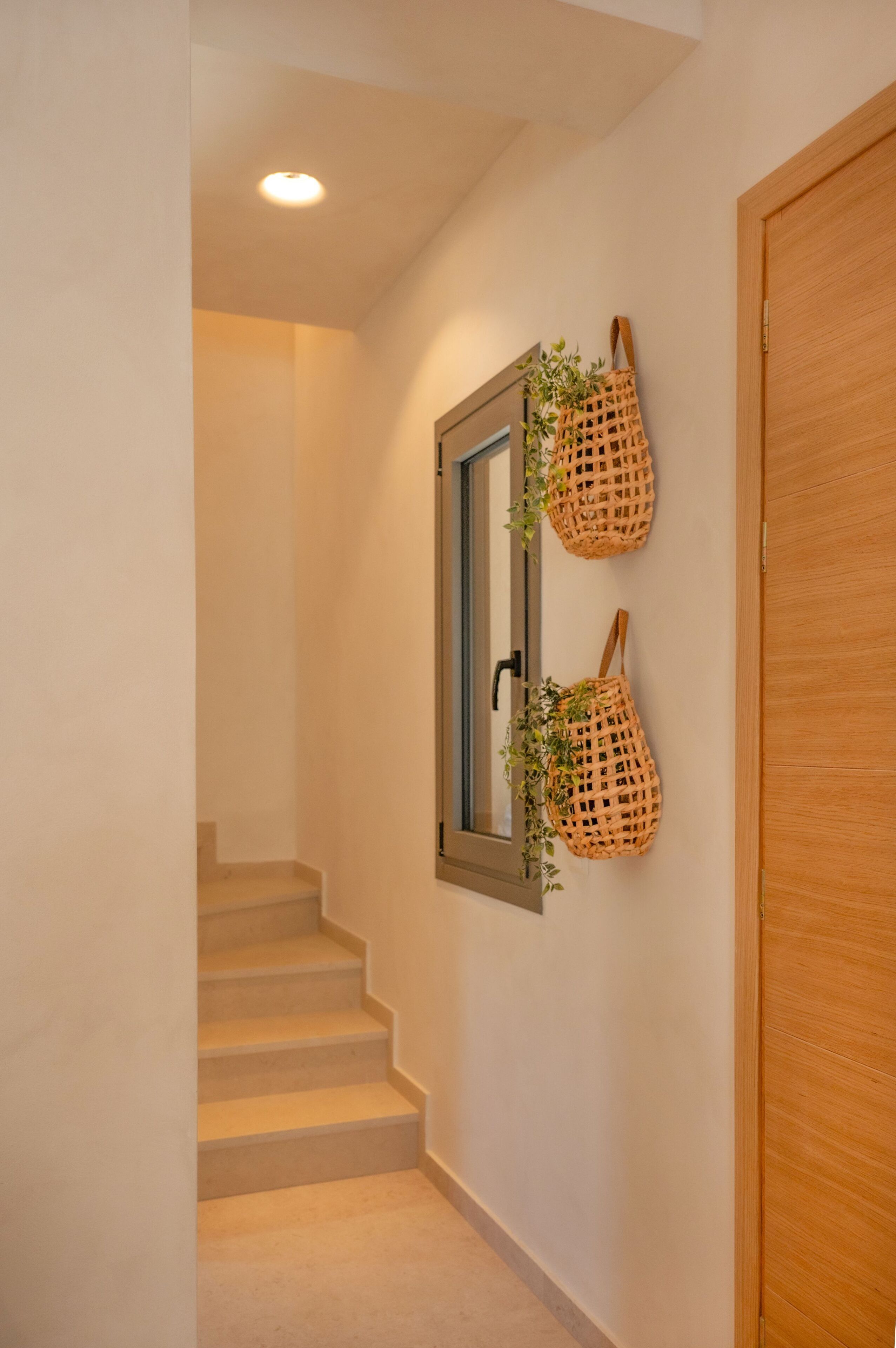 Una escalera con una puerta de madera a la derecha y un espejo fijado a la pared, con dos cestas tejidas colgando.