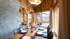 Comedor con pared de piedra, vigas de madera y grandes ventanas con vistas a la montaña.