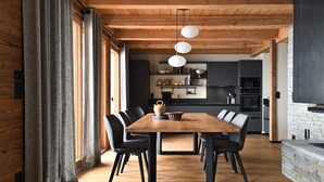 A modern kitchen with dark cabinetry, a wooden dining table, and black chairs. - Vue exceptionnelle ! Chalet moderne + sauna privé (Les Deux Alpes)
