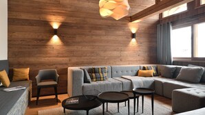 A cozy living room with a wooden ceiling, a sectional sofa, a round coffee table, and two wall-mounted lamps. - Vue exceptionnelle ! Chalet moderne + sauna privé (Les Deux Alpes)