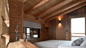 A wooden cabin room with a bed, a small table, a window, and a wall-mounted light fixture. - Vue exceptionnelle ! Chalet moderne + sauna privé (Les Deux Alpes)