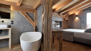 A modern bathroom with a large white bathtub, wooden beams, and a stone wall. - Vue exceptionnelle ! Chalet moderne + sauna privé (Les Deux Alpes)