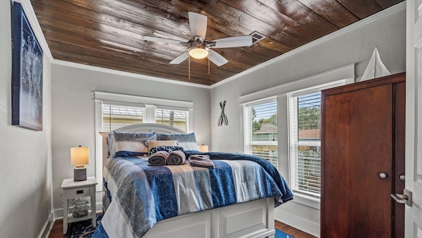 Une chambre à coucher avec un lit, un ventilateur de plafond, une table de chevet, une fenêtre et une porte.