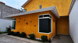 A modern yellow building with a flat roof, a large window, and a small door. - Casa Santa Cecilia (Tehuacán)