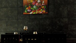 A dining area with a table set for two, a painting of fruits and flowers on the wall, and a dark textured wall. - Casa Santa Cecilia (Tehuacán)
