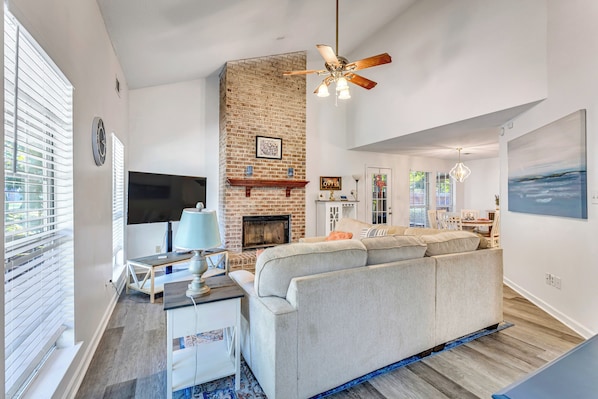 A living room with a brick fireplace, a ceiling fan, and a large window with blinds. - New Listing Promo + Cruising the Coast (Ocean Springs)