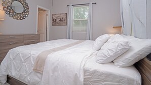 Un dormitorio con cama, cómoda, espejo y ventana con persianas.