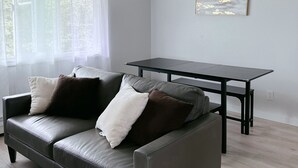 A modern living room with a grey leather sofa, a small black table, and a white wall with a framed abstract painting.