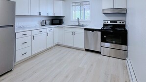 A modern kitchen with white cabinets, a stainless steel refrigerator, a microwave, a sink, a stove, and a ceiling fan.