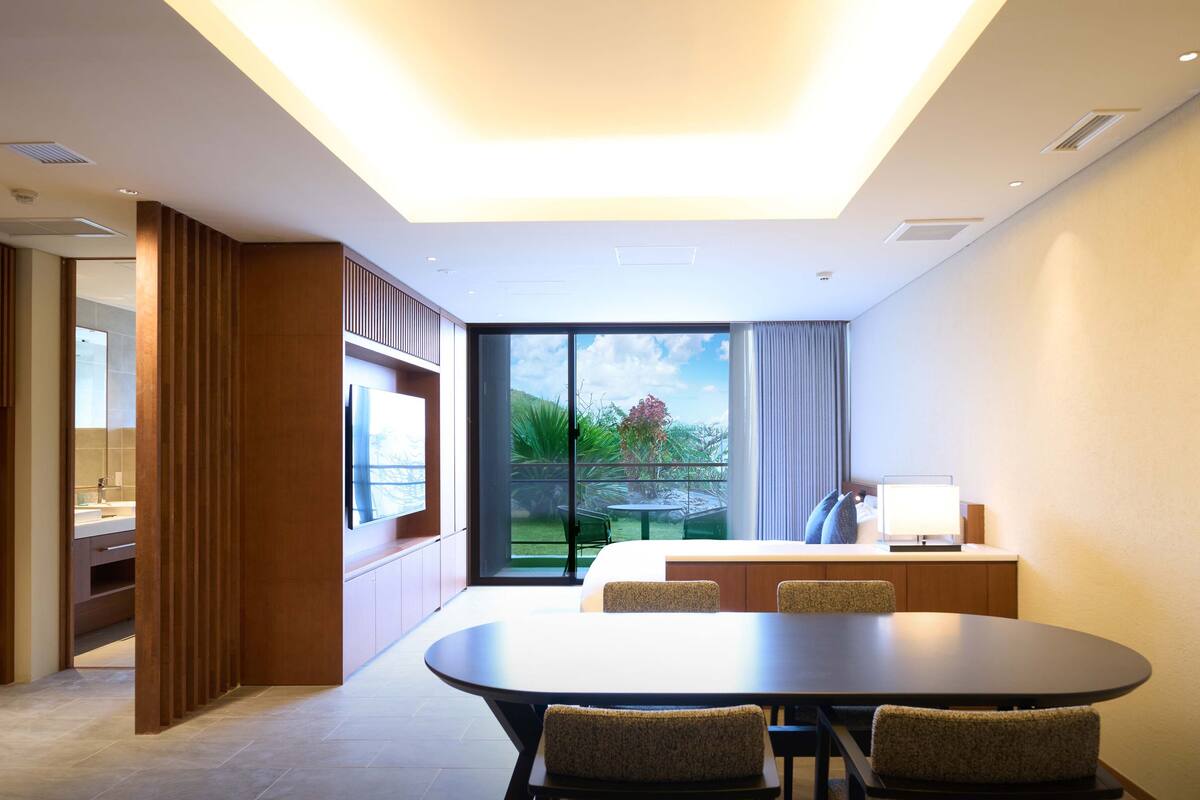 Une chambre d’hôtel moderne dotée d’un coin repas, d’une grande fenêtre donnant sur l’extérieur et d’une kitchenette.
