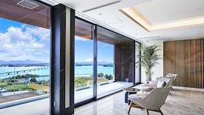 A modern room with large windows, a view of a bridge and water, and a seating area with a plant. - BATON SUITE Okinawa Kouri Island (Nakijin)