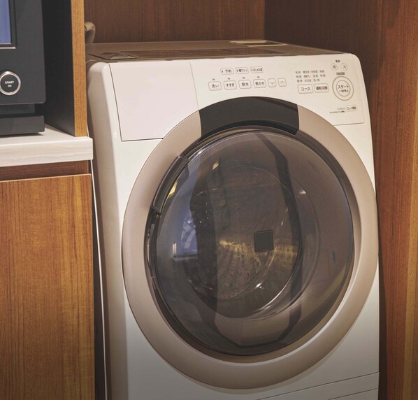 A front-loading washing machine with a control panel, located in a wooden cabinet. - BATON SUITE Okinawa Kouri Island (Nakijin)