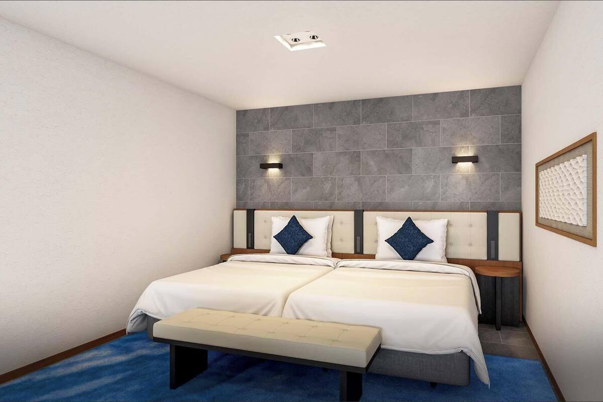 Un lit double avec une banquette, deux tables de chevet, une lampe fixée au mur et un panneau mural texturé.