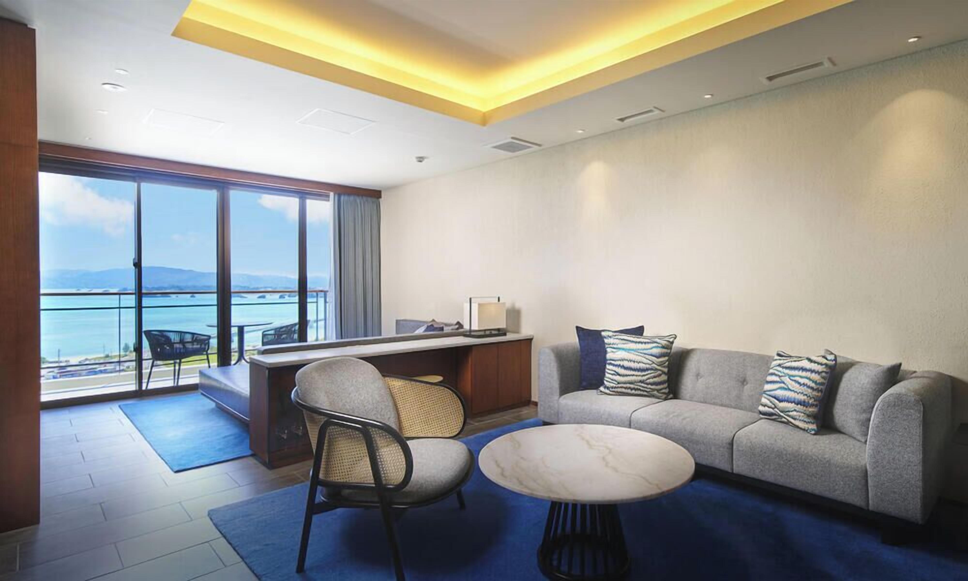 Ein modernes Hotelzimmer mit Balkon, einer Couch, einem Couchtisch und einem Schreibtisch.