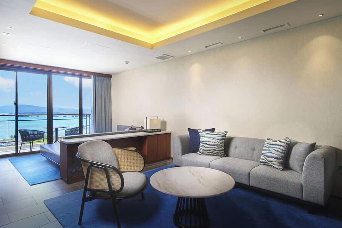 A modern hotel room with a balcony, a sofa, a coffee table, and a desk.