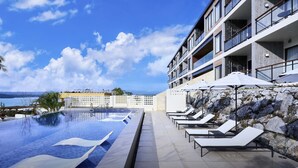A modern hotel with a pool, lounge chairs, and a view of the sea. - BATON SUITE Okinawa Kouri Island (Nakijin)