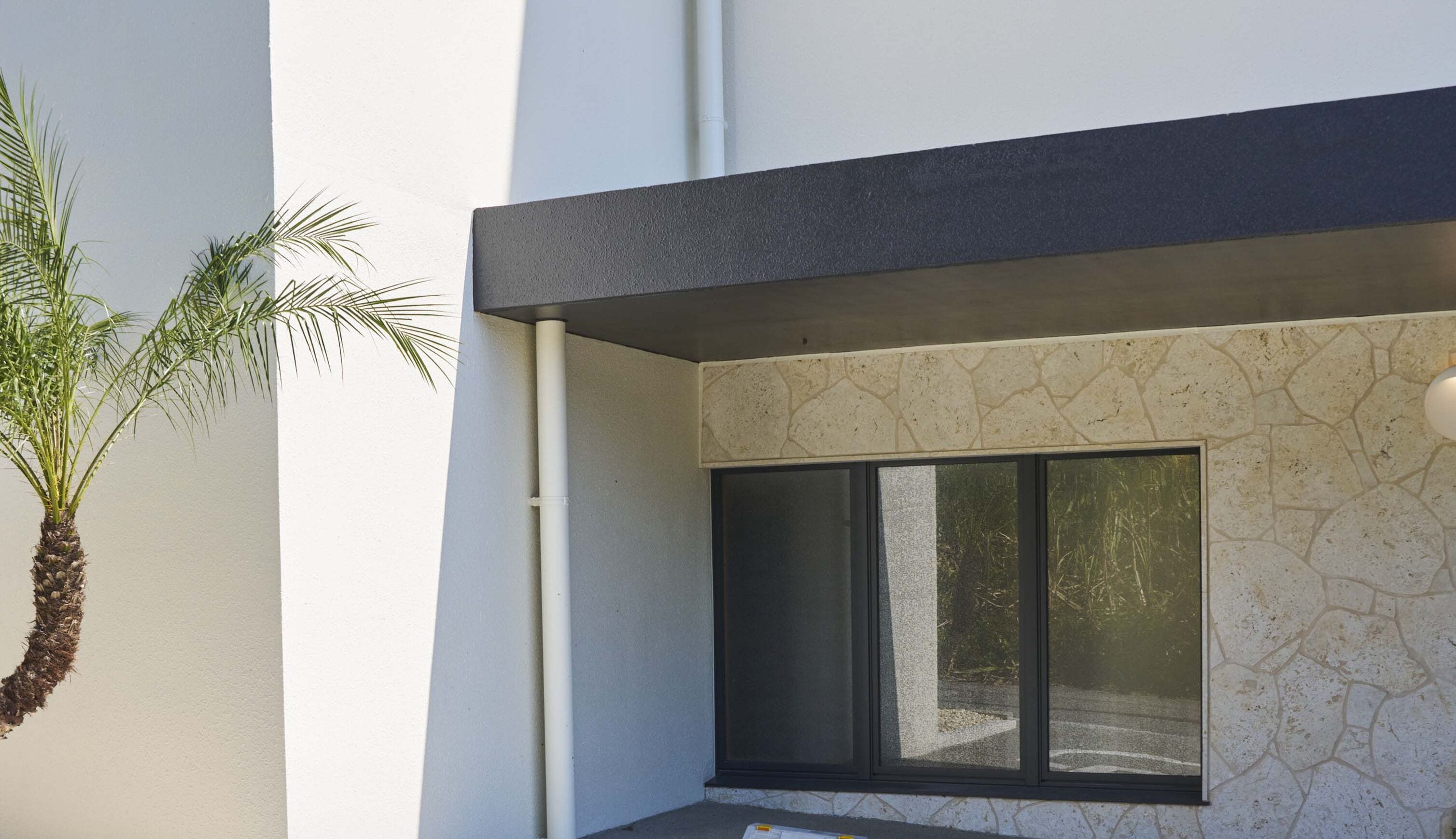 Een modern gebouw met een gevel van natuursteen, een groot raam en een palmboom.