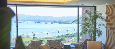 A modern room with large windows, wicker furniture, and a view of a coastal landscape with a bridge.