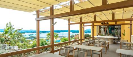 An outdoor patio with wooden tables and chairs, a covered area with a view of a bridge and water.