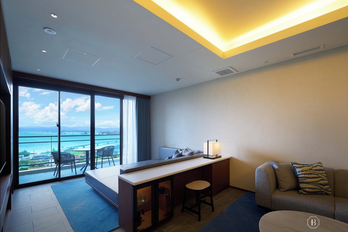 Une chambre d’hôtel moderne dotée d’un balcon, d’un bureau, d’un canapé et offrant une vue sur l’océan.