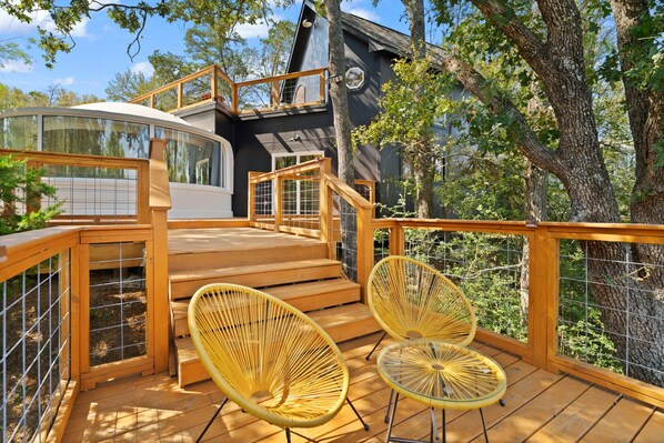 A modern house with a wooden deck, two yellow wicker chairs, and a staircase leading to a second level.