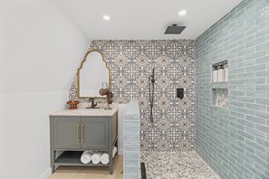 A bathroom with a grey vanity, patterned tiles, and a shower area.