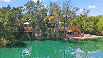 A cabin with a deck overlooking a body of water, surrounded by trees.
