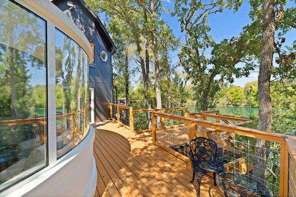 A wooden deck with a glass enclosure, surrounded by trees and a lake view.