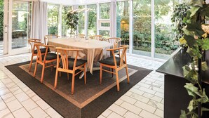 Een eetgedeelte met een ronde tafel, zes houten stoelen en een groot raam met uitzicht op groen.