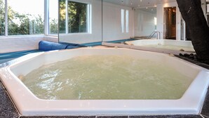 Een wellnessruimte met een ruime jacuzzi en een zithoek bij een raam.