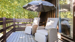 Een houten terras met rieten stoelen en een witte parasol.