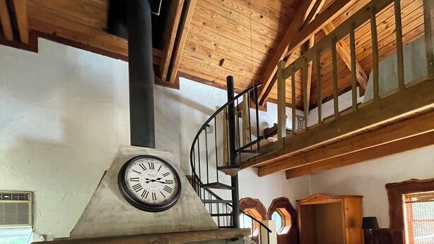 A spacious living room with a stone fireplace, a wooden staircase, and a high ceiling.