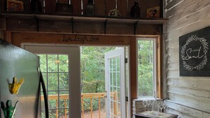 A wooden cabin interior with a door leading to a deck, a refrigerator, and a small table with wine glasses.