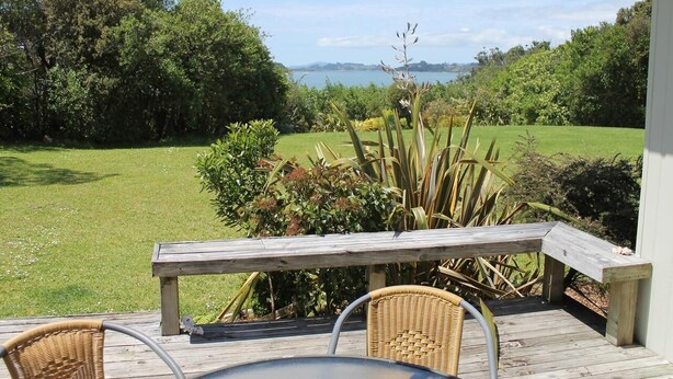 A deck with a table and chairs, overlooking a grassy area with trees and a body of water in the distance. - Private Island Eco Retreat complete with resident Kiwi (Kerikeri)